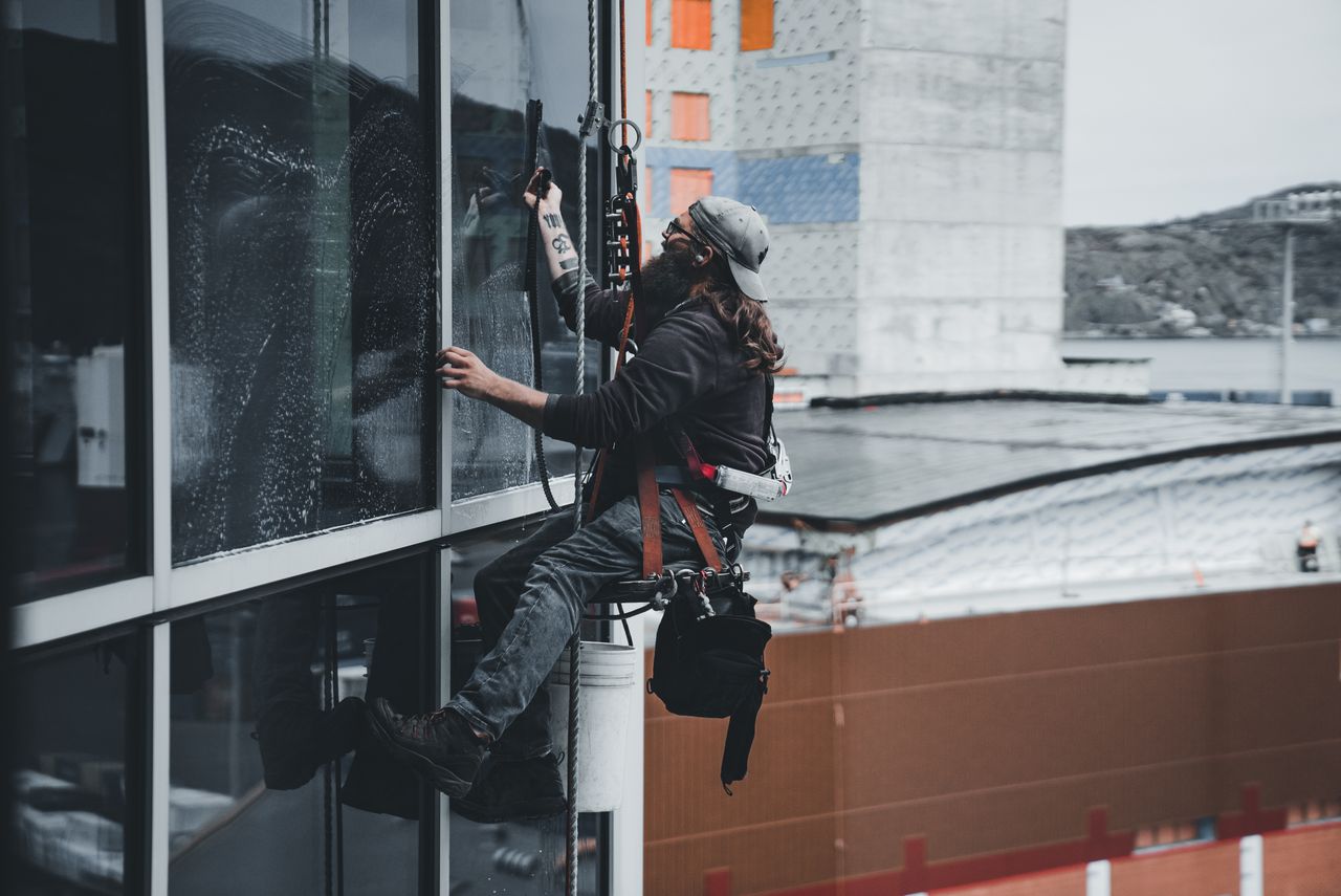 project-02-b A man washing the windows of a skyscraper while secured in a harness, highlighting work performed on tall urban buildings.